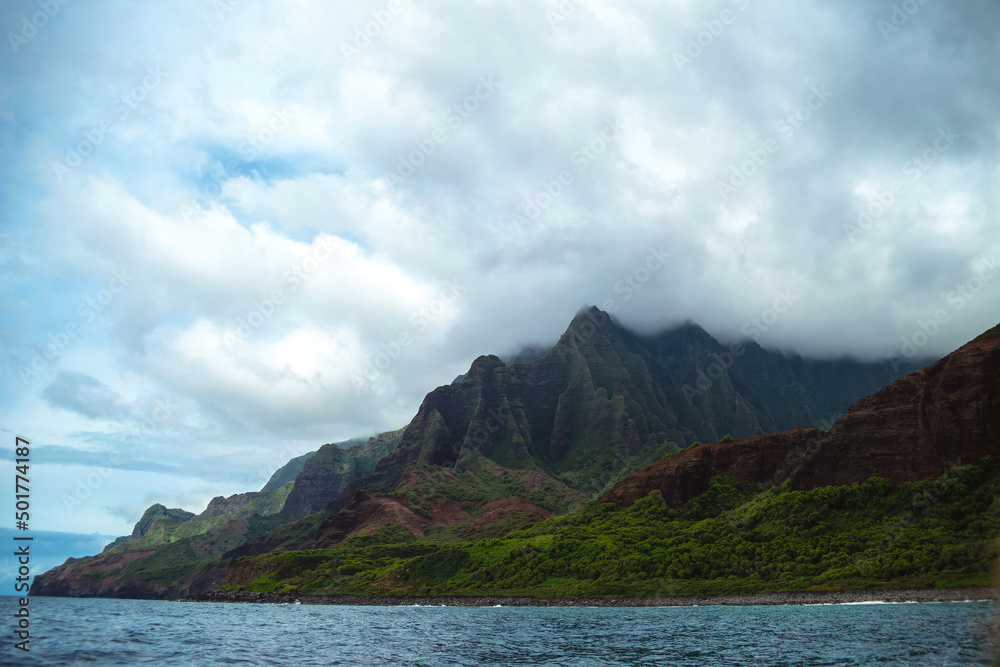 The gorgeous rugged wilderness and cliffs of Kauai's Napali Coast in Hawaii, with low clouds and mist hanging over the mountain peaks under a stormy grey sky, and bright blue and teal ocean waves The gorgeous rugged wilderness and cliffs of Kauai's Napali Coast in Hawaii, with low clouds and mist hanging over the mountain peaks under a stormy grey sky, and bright blue and teal ocean waves