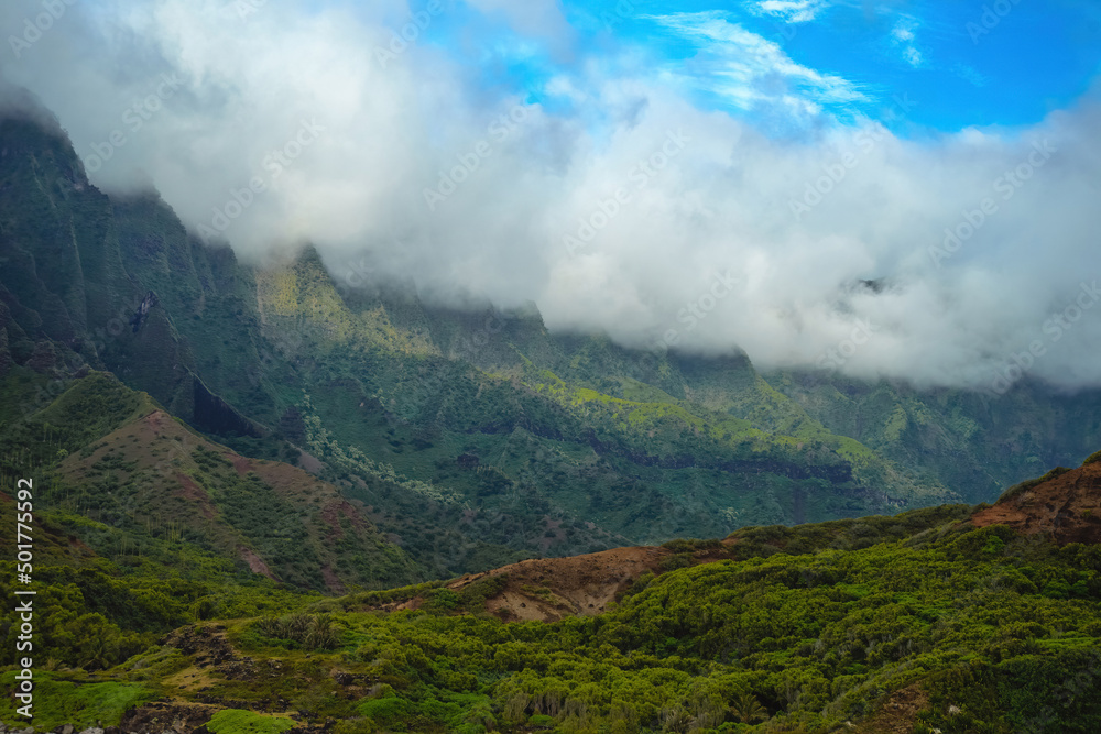 The gorgeous rugged wilderness and cliffs of Kauai's Napali Coast in Hawaii, with low clouds and mist hanging over the mountain peaks under a stormy grey sky