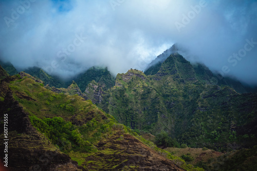The gorgeous rugged wilderness and cliffs of Kauai s Napali Coast in Hawaii  with low clouds and mist hanging over the mountain peaks under a stormy grey sky