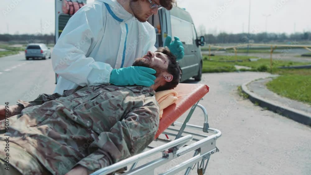 Close up medic provides first aid to wounded soldiers scream in pain in wheelchairs near ambulance. Military concept. War. Outdoors. Close up medic provides first aid to wounded soldiers scream in pain in wheelchairs near ambulance. Military concept. War. Outdoors.