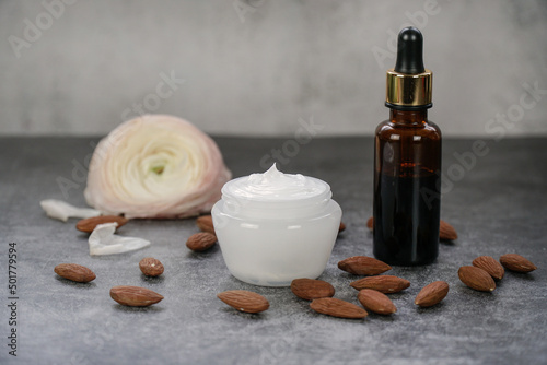              Sweet almond oil and  almond face or body cream with almonds on grey background with real flowers.     