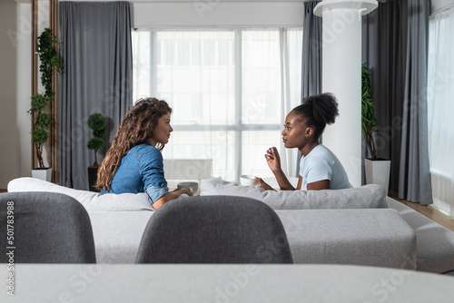 Two young friends and roommates sitting on sofa in their modern cozy studio apartment talking about men. Females conversation about relationships and goals for the future. photo
