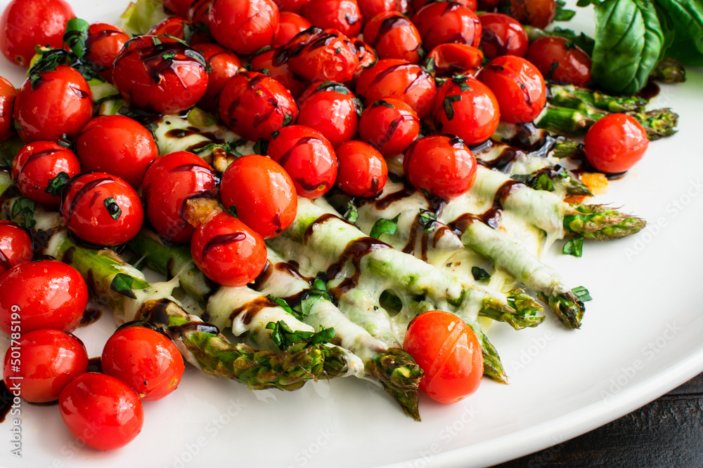 Closeup View of Caprese Roasted Asparagus: Roasted asparagus and grape tomatoes topped with mozzarella cheese and balsamic glaze Closeup View of Caprese Roasted Asparagus: Roasted asparagus and grape tomatoes topped with mozzarella cheese and balsamic glaze