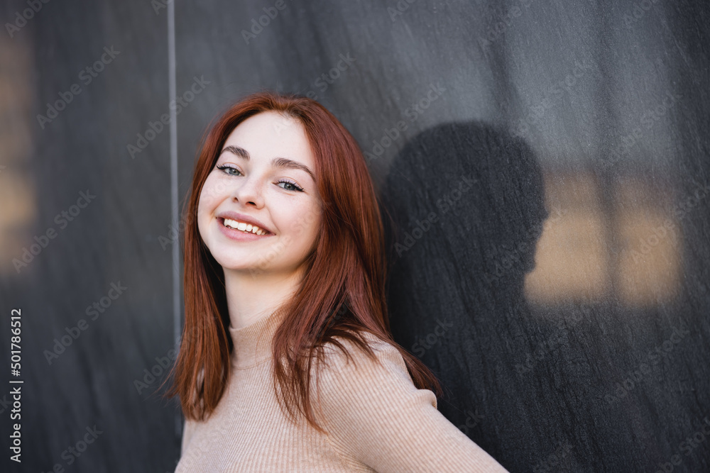 happy redhead woman in beige turtleneck smiling near grey marble wall. happy redhead woman in beige turtleneck smiling near grey marble wall.