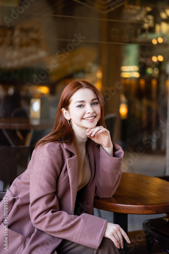 young and happy woman with red hair sitting in cafe terrace.