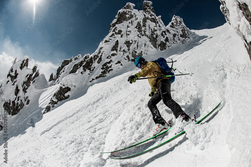 Skier dressed in beige and black sportswear with go-pro camera oh his helmet sliding down snow-covered slopes