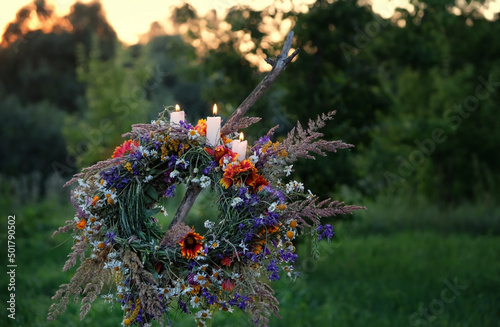 Flower wreath with burn candles on evening meadow. Summer Solstice Day, Midsummer concept. floral traditional festive decor. pagan witch traditions, wiccan symbolic rituals