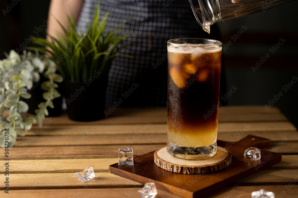 Glass of espresso with lemon juice on wooden table and copy space, Summer Cocktail, Cold brew coffee or black tea. (close up, selective focus),Pouring cold drink. Glass of espresso with lemon juice on wooden table and copy space, Summer Cocktail, Cold brew coffee or black tea. (close up, selective focus),Pouring cold drink.