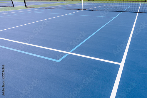 Close up photo of new outdoor blue tennis court with white lines combined with light blue pickleball lines.