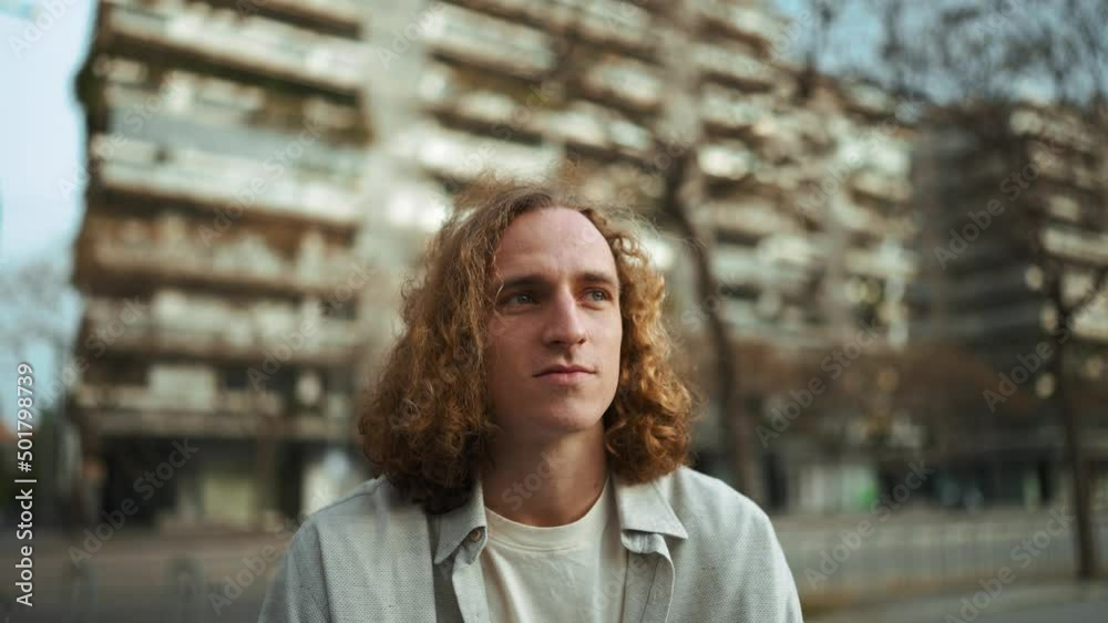Positive curly-haired man looking at the view while sitting on the bench outdoors Positive curly-haired man looking at the view while sitting on the bench outdoors