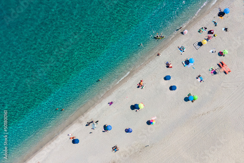 Spiaggia con acqua azzurra, sabbia bianca e ombrelloni colorati. Ripresa dall'alto.
