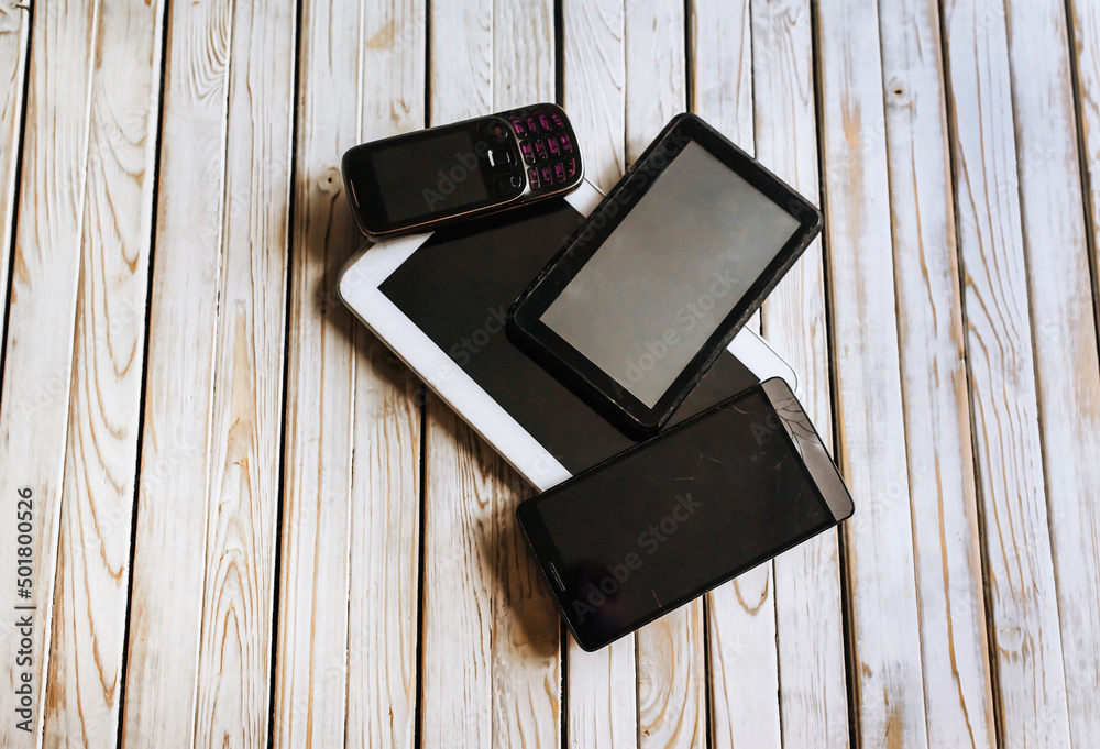 Old broken gadgets, smartphones lie on a wooden background. Old broken gadgets, smartphones lie on a wooden background.
