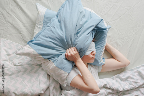 woman lies in bed and covers her head with pillows. the woman suffers from insomnia or sleep disorders. noise prevents you from sleeping at night. a tired woman can't sleep. depression and sleep