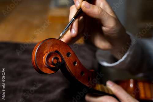 young chinese woman violin maker finishing painting a violin with a thin brush