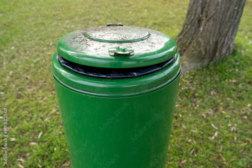 Green round metal garbage can in the park Green round metal garbage can in the park