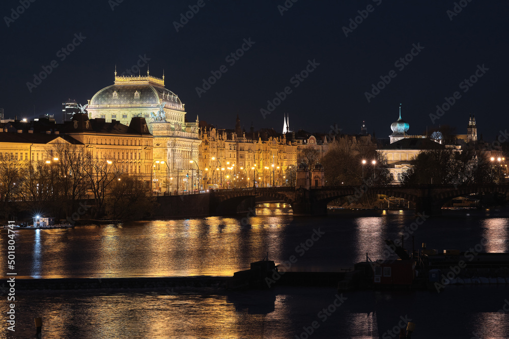 The National Theater in Prague at night with the Vltava river. Reflections of the National Theatre in Prague on the Vltava River. View from Charles Bridge in Prague. Prague, Czech Republic.