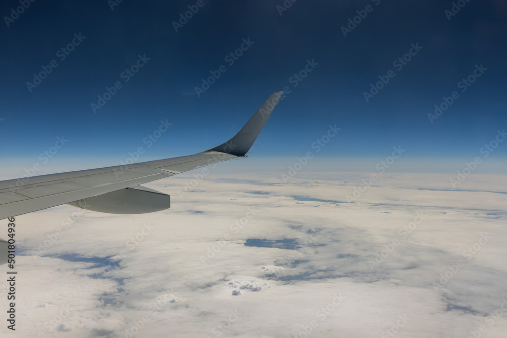 Obraz premium Flying traveling view from airplane window on the wing on clouds blue sky background