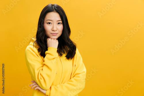 Hmm. Thoughtful pensive Asian student young woman in yellow hoodie reclines on fist think about education problems posing isolated on over orange studio background. Cool offer. People Emotions concept © SHOTPRIME STUDIO