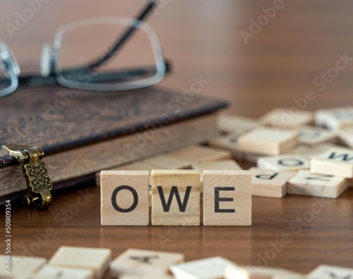 owe word or concept represented by wooden letter tiles on a wooden table with glasses and a book