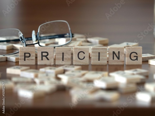 pricing word or concept represented by wooden letter tiles on a wooden table with glasses and a book photo