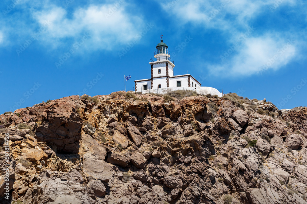 The old lighthouse on the rocky sea coast. Blue sky with clouds.