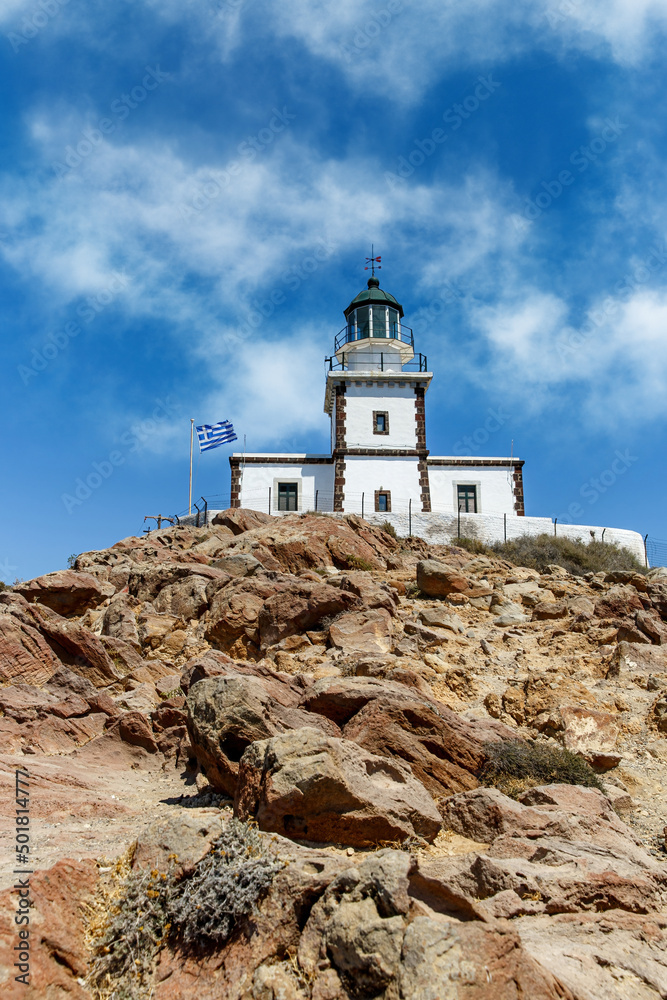 The old lighthouse on the rocky sea coast. Blue sky with clouds.