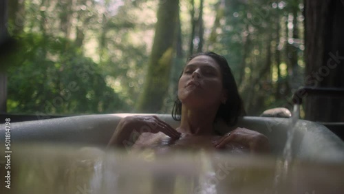 A girl in a bathtub in a forest during the rain. Beautiful young woman relaxing in the bathroom in the tropical rainforest jungle in a luxury spa while raining
