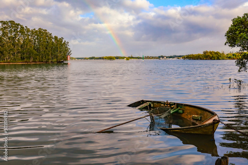 Tranquil water scene with partially sunk row boat in Wallis Lake at Forster NSW with rainbow in background photo