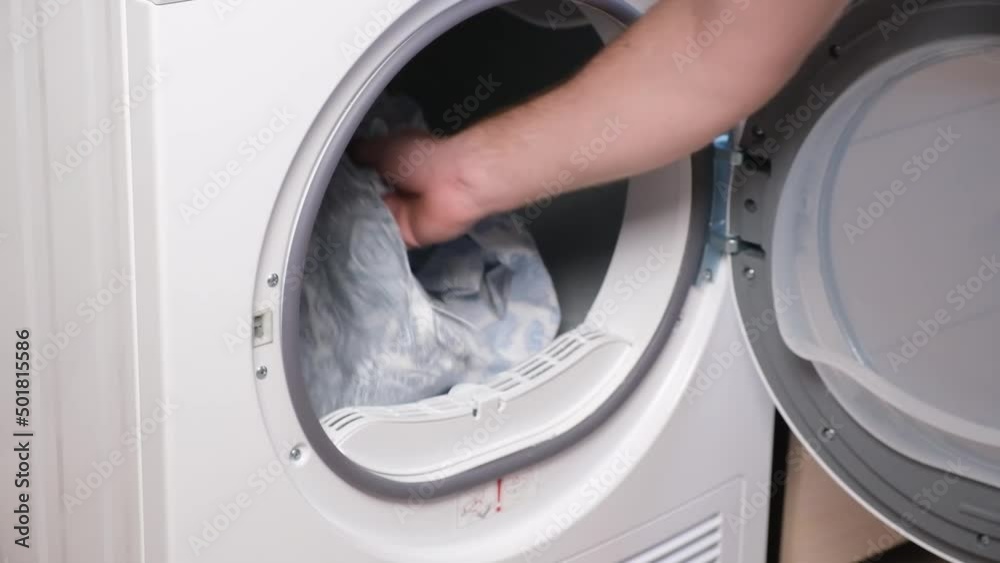 A man takes dried bed linen out of the dryer. Dryer machine in the house. A man takes dried bed linen out of the dryer. Dryer machine in the house.