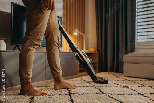 Lowsection of man hoovering carpet with vacuum cleaner in living room photo