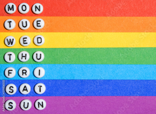 Three letter days of the week: Mon Tue Wed Thu Fri Sat Sun. Isolated on rainbow background: red, orange, yellow, green, cyan, indigo, purple colors. Stripes for notes. Empty place. Copy space