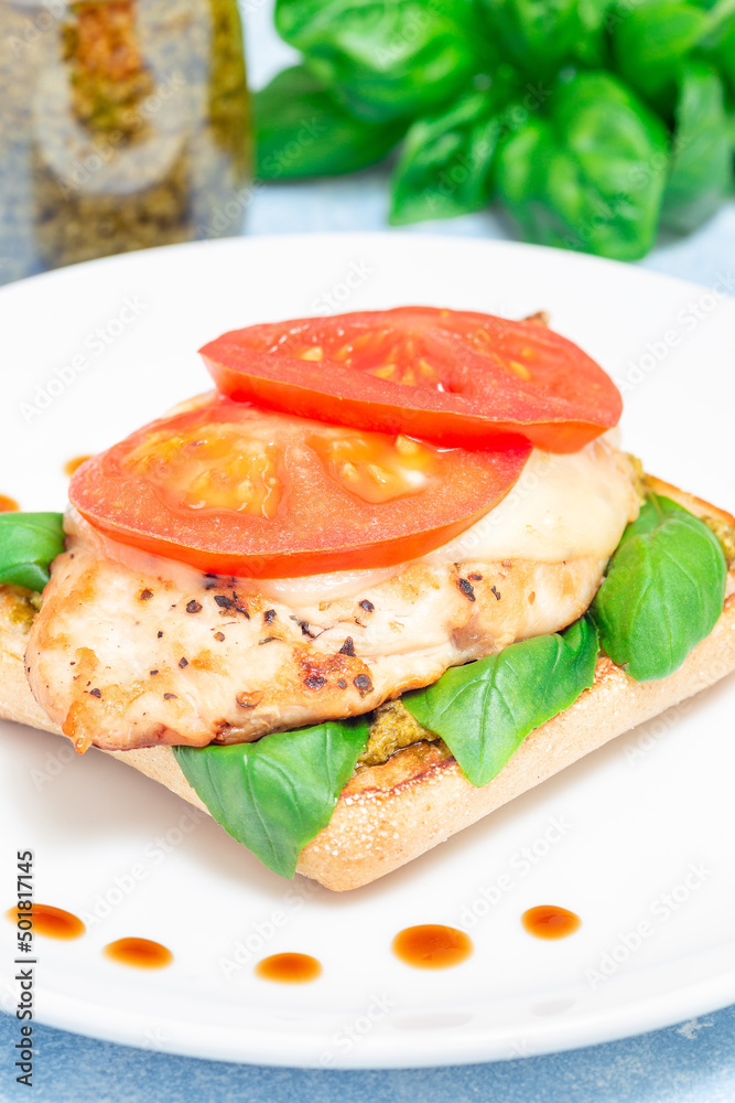 Sandwich with chicken, mozzarella, tomato, pesto and basil on toasted ciabatta, vertical