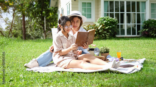 Mother and daughter having picnic, reading book together at outdoors. Summer Weekend Concept