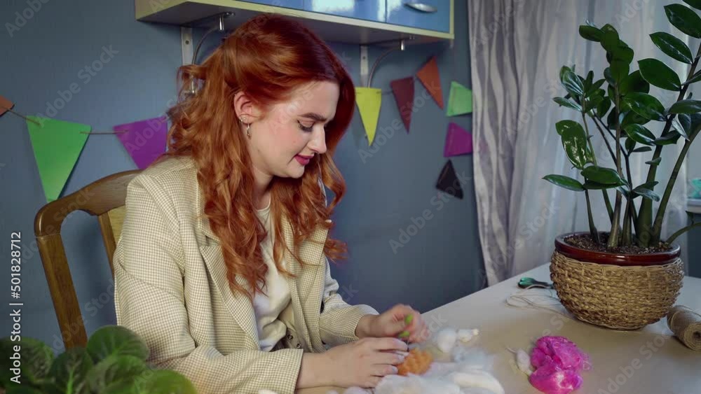 A beautiful red-haired girl, she rolls wool and creates toys. The girl was pricked with a wool felting needle. Handmade work A beautiful red-haired girl, she rolls wool and creates toys. The girl was pricked with a wool felting needle. Handmade work