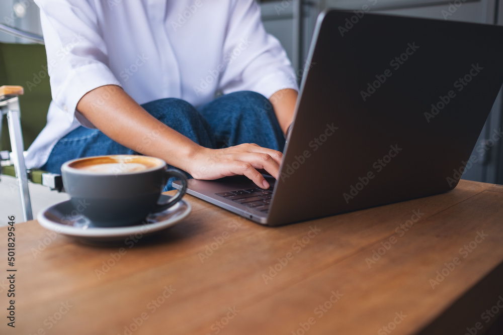 Closeup image of a woman working and typing on laptop computer keyboard with coffee cup on the table Closeup image of a woman working and typing on laptop computer keyboard with coffee cup on the table