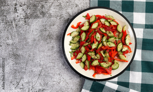 Cucumbers, bell pepper and herbs fresh healthy salad on a round plate on a dark gray background. Top view, flat lay