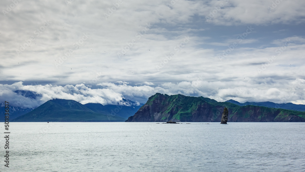 The picturesque coast of Kamchatka against the sky. Low clouds hide the peaks of the mountains. A lonely cliff in the Pacific Ocean. Avacha Bay