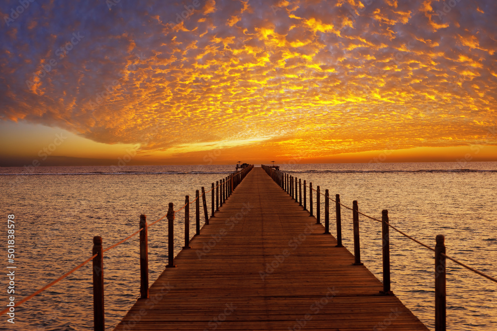 Obraz premium orange sky with spindrift clouds on sunrise in Egypt and wooden bridge in sea