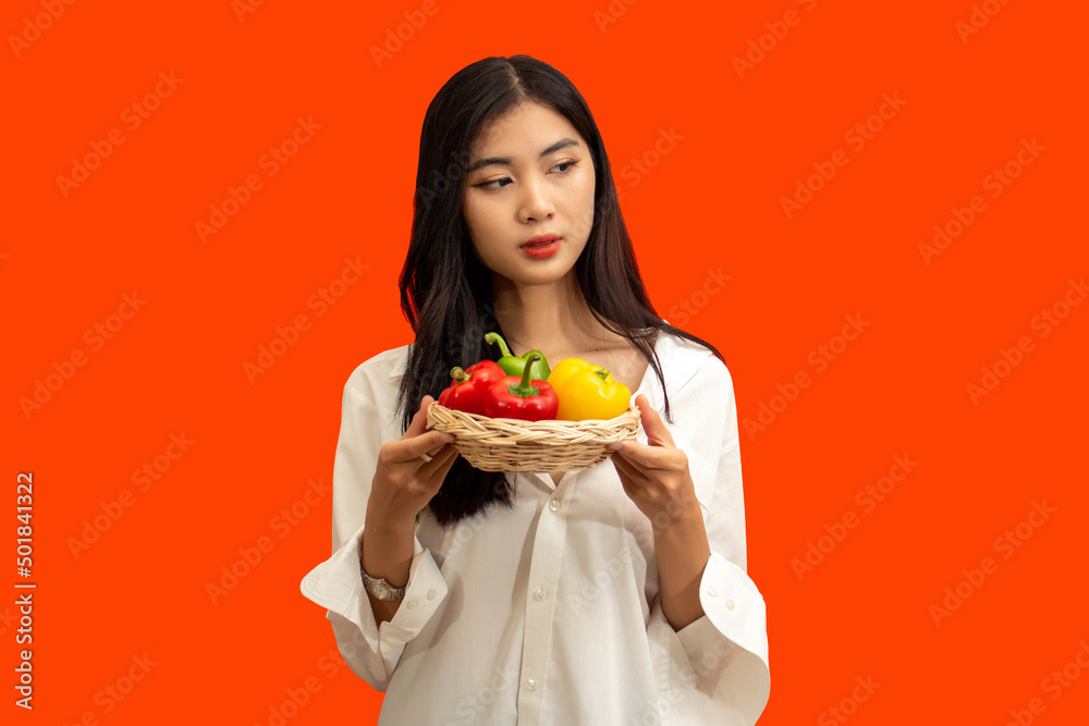 Vegetarian concept, Healthy woman hold basket of colorful bell pepper isolated on orange background Vegetarian concept, Healthy woman hold basket of colorful bell pepper isolated on orange background