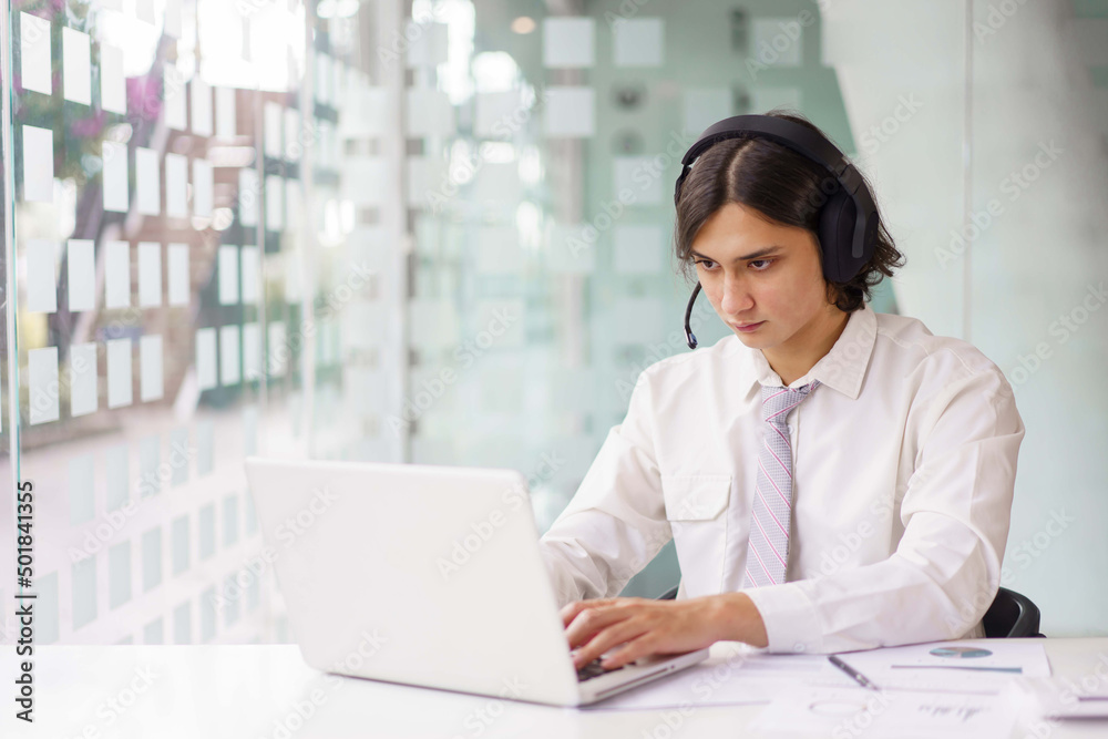 Business concept, Businessman wearing headphone and typing data on laptop while video conference Business concept, Businessman wearing headphone and typing data on laptop while video conference