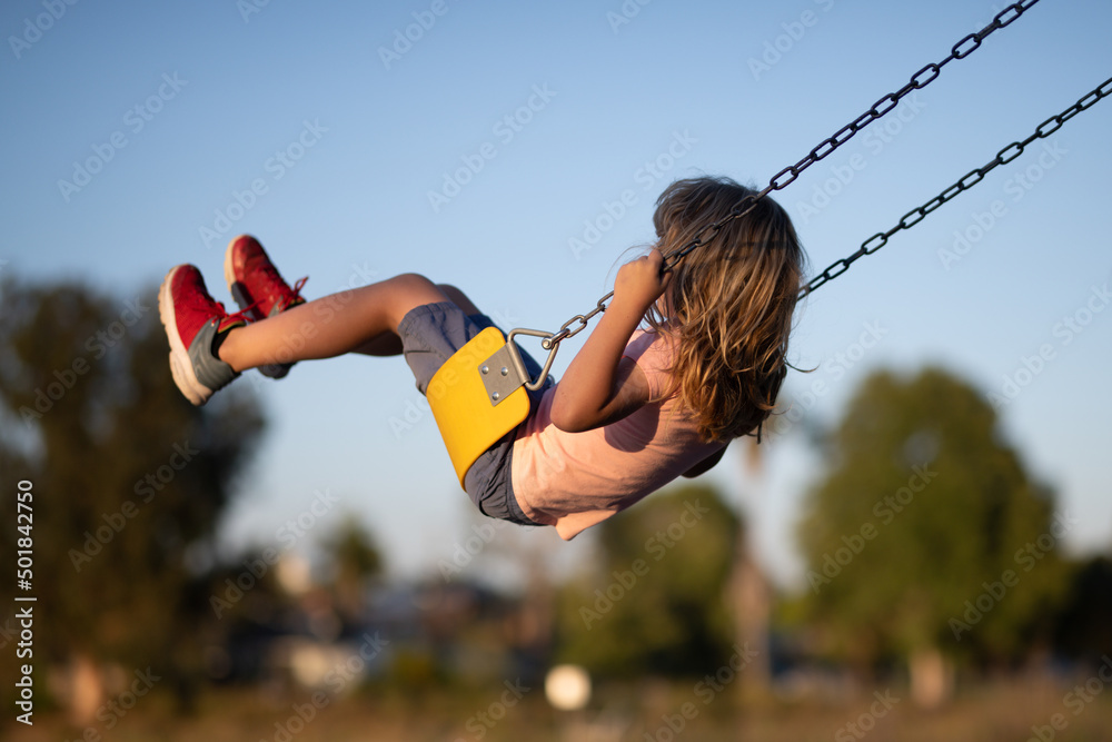 Little boy having fun on a swing on the playground in public park on summer day. Happy child enjoy swinging. Child playing on outdoor playground. Kids play on kindergarten yard. - obrazy, fototapety, plakaty 