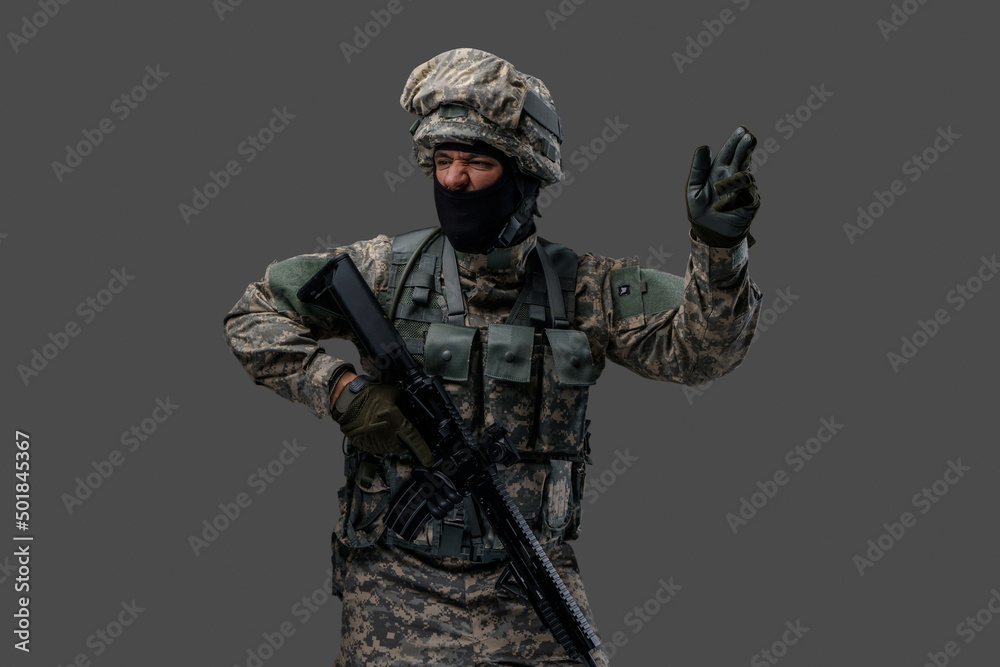 Proud serviceman dressed in camouflage clothes with rifle gesturing against grey background. Proud serviceman dressed in camouflage clothes with rifle gesturing against grey background.