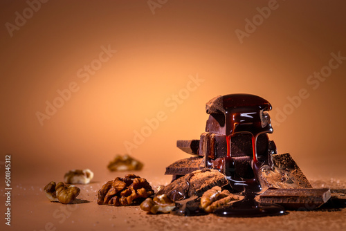 A stack of dark broken chocolate drizzled with melted chocolate and walnuts on a bright orange background. Copy space