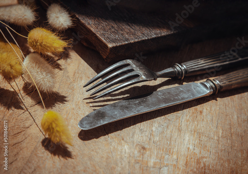 Vintage old metal knife with fork and Dried rabbit tail grass flowers on old rustic wooden table. Eating concept, Copy space, Selective Focus.