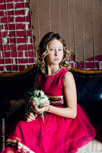 a girl in a red dress is sitting on the sofa and holding a bouquet of flowers in her hands