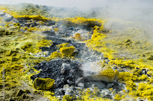 Yellow Sulphur on surface of rocks on top of a volcano crater on the island of Vulcano  Aeolian Archipelago. Sicily  Italy. Gray white and Yellow background of Sulfur. Steam and smoke from fumarole 