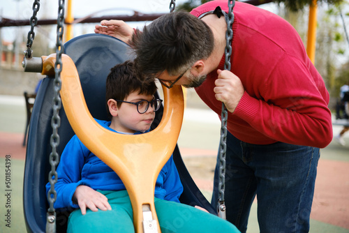 Slika na platnu A disabled boy and his father enjoy playing in the park playground with a special needs swing