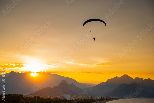 Silhouette of a man on a paraglider flying over the sea at sunset.