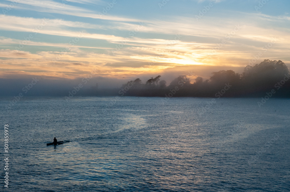 Silhoutte of a person in a kayak peddling in the Santa Cruz bay during sunset.