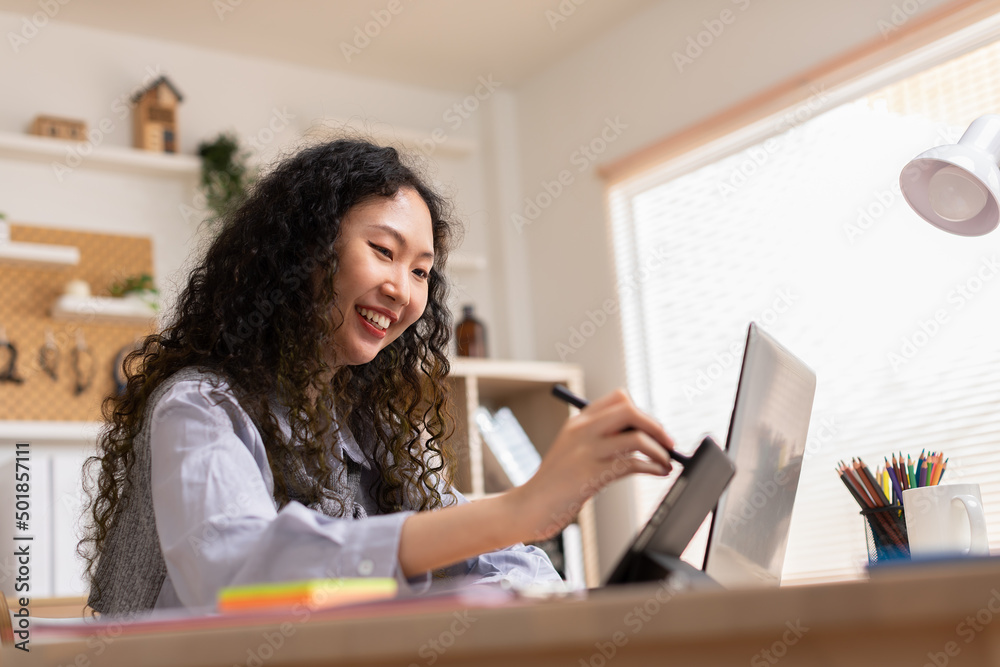 Asian young creative or graphic designer with curly hairstyle drawing or sketching on digital tablet smiling at home.Happiness female freelancer smart and confident enjoying with job or work Asian young creative or graphic designer with curly hairstyle drawing or sketching on digital tablet smiling at home.Happiness female freelancer smart and confident enjoying with job or work